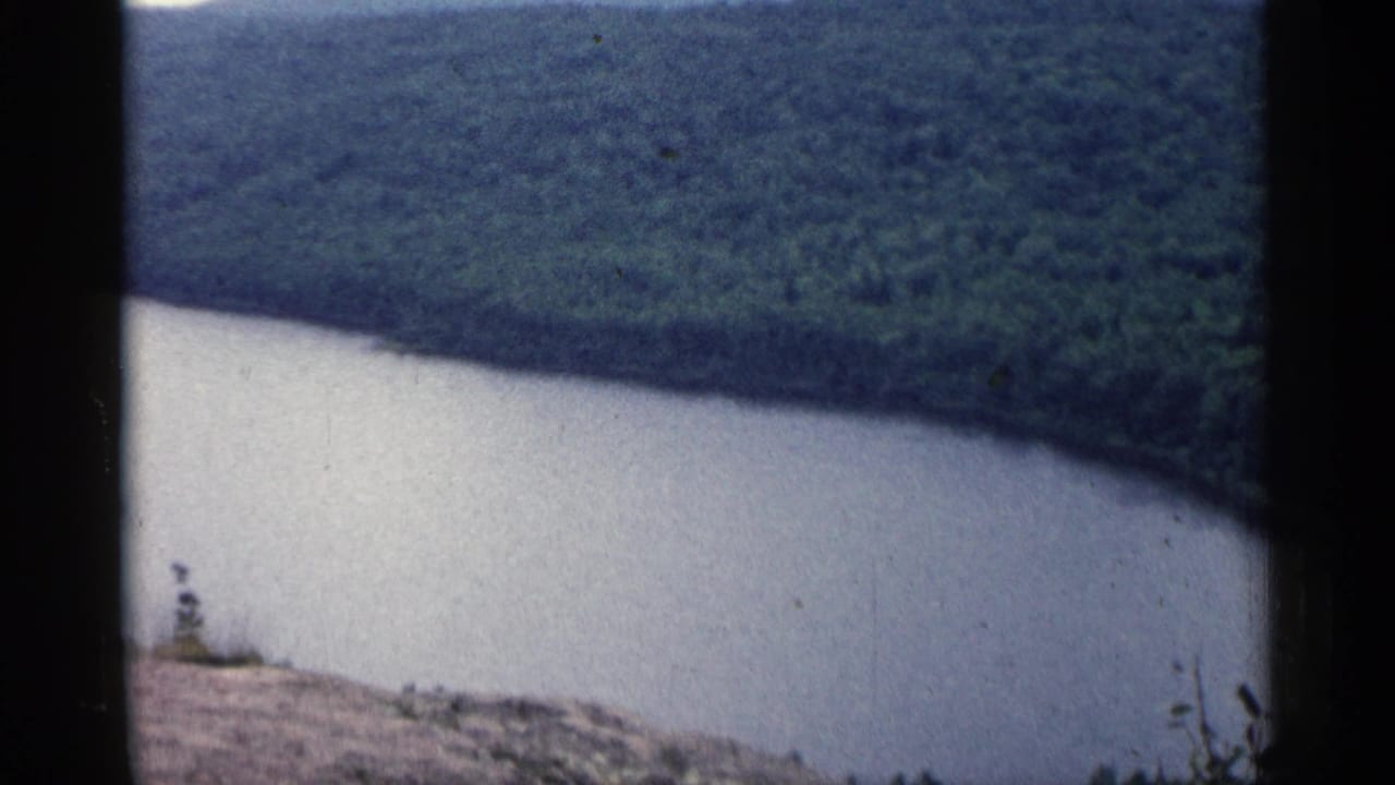 1960 Michigan 8mm frame showing a broad river curve beneath wooded hills from a rocky hillside overlook.