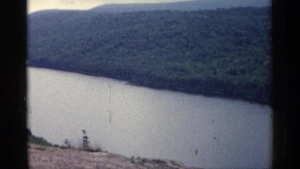 Vintage 8mm frame of a Michigan river below wooded hills, with soft focus and a muted color palette.