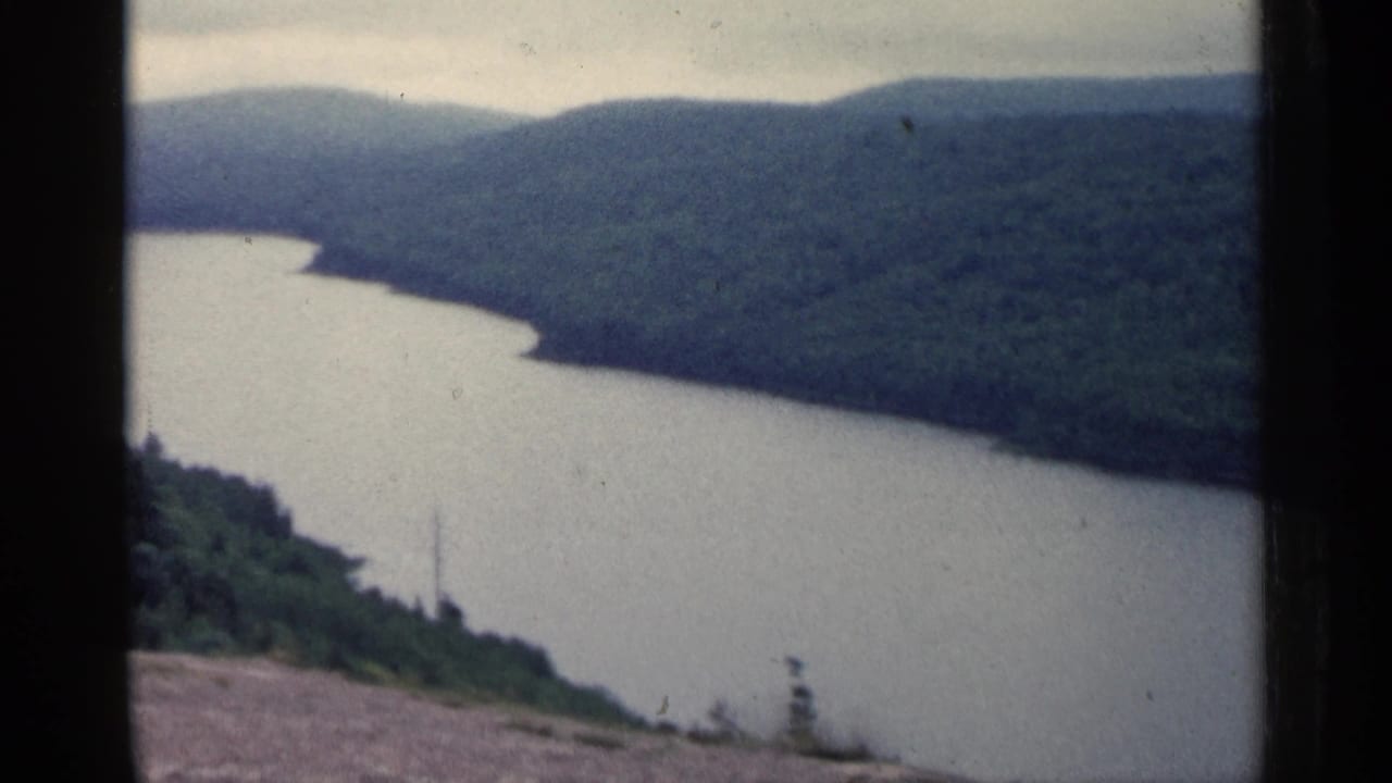 1960 Michigan 8mm frame showing a winding river or lake inlet seen from a high wooded overlook.