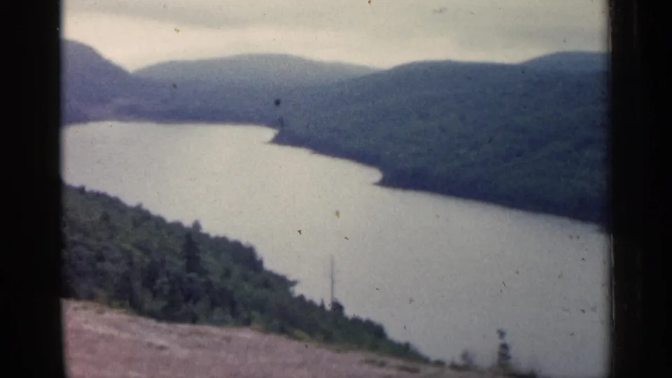 Vintage 8mm still from Michigan showing a hillside viewpoint over water and continuous forest cover.