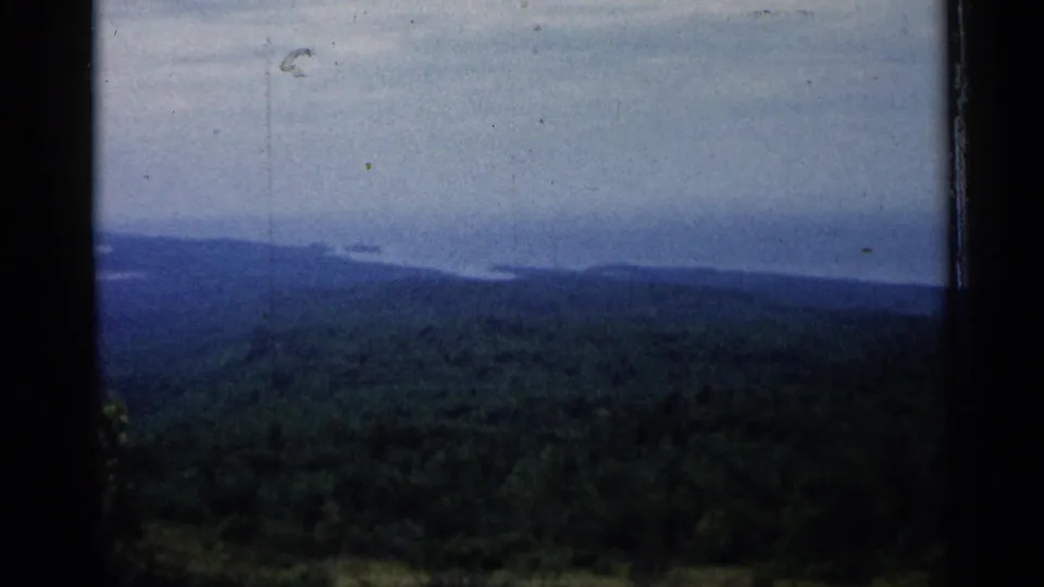 1960 Michigan 8mm view of green forested hills leading toward distant blue lake water under a pale sky.
