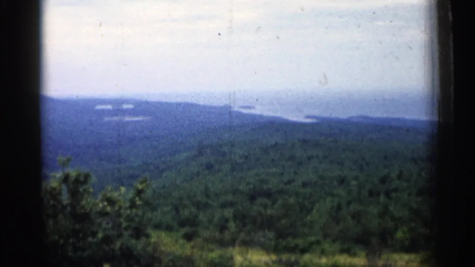 1960 Michigan home-movie frame with layered green hills, distant shoreline or islands, and dark 8mm frame borders.