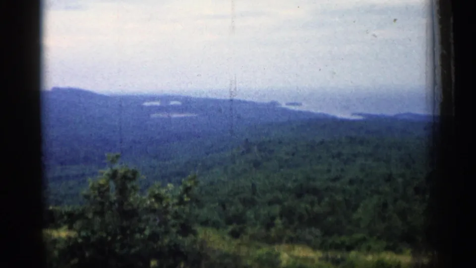 1960 Michigan 8mm frame showing a soft, hazy view across green hills toward a distant body of water.