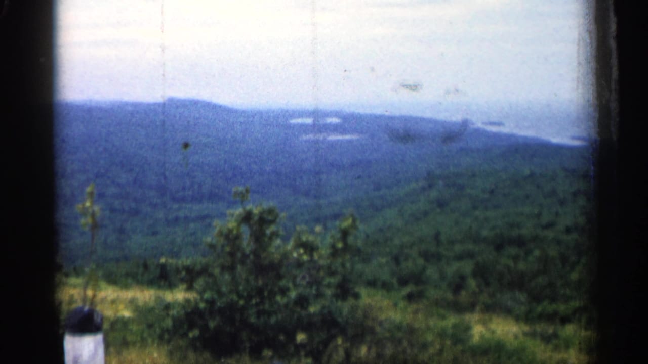 Forested hills under a cloudy sky, framed by dark film or window edges.
