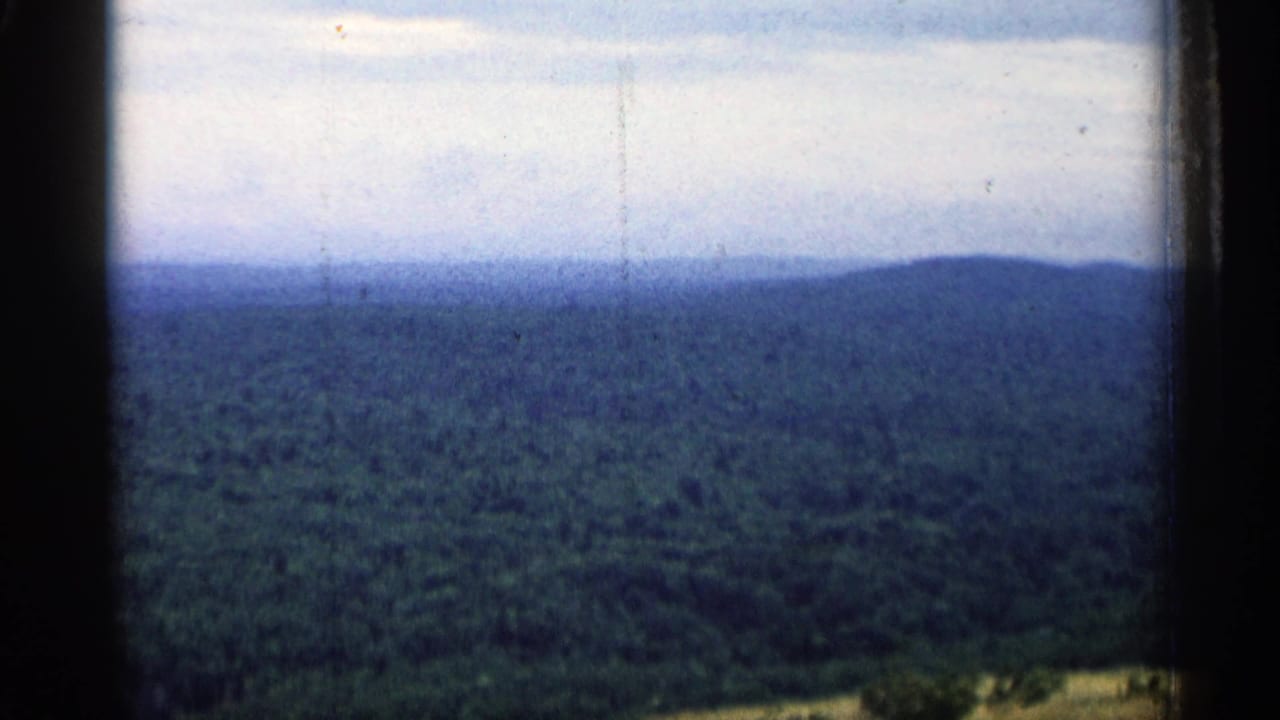 1960 Michigan 8mm view of a broad wooded landscape and low distant hills seen through dark window-like frame edges.