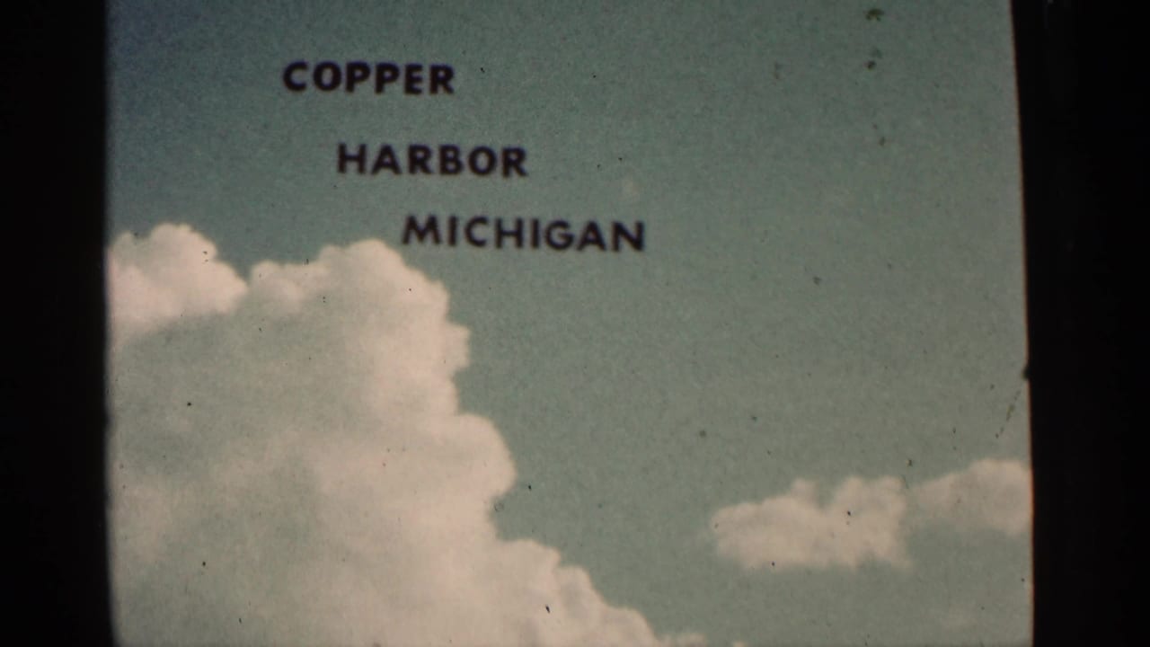 1960 8mm title frame reading Copper Harbor Michigan against pale blue sky and clouds, with visible film gate edges and grain.
