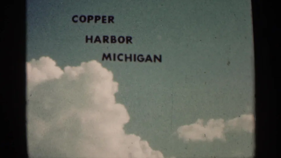Title card for Copper Harbor, Michigan holds over clouds and blue sky in faded 8mm color, framed by dark gate edges.