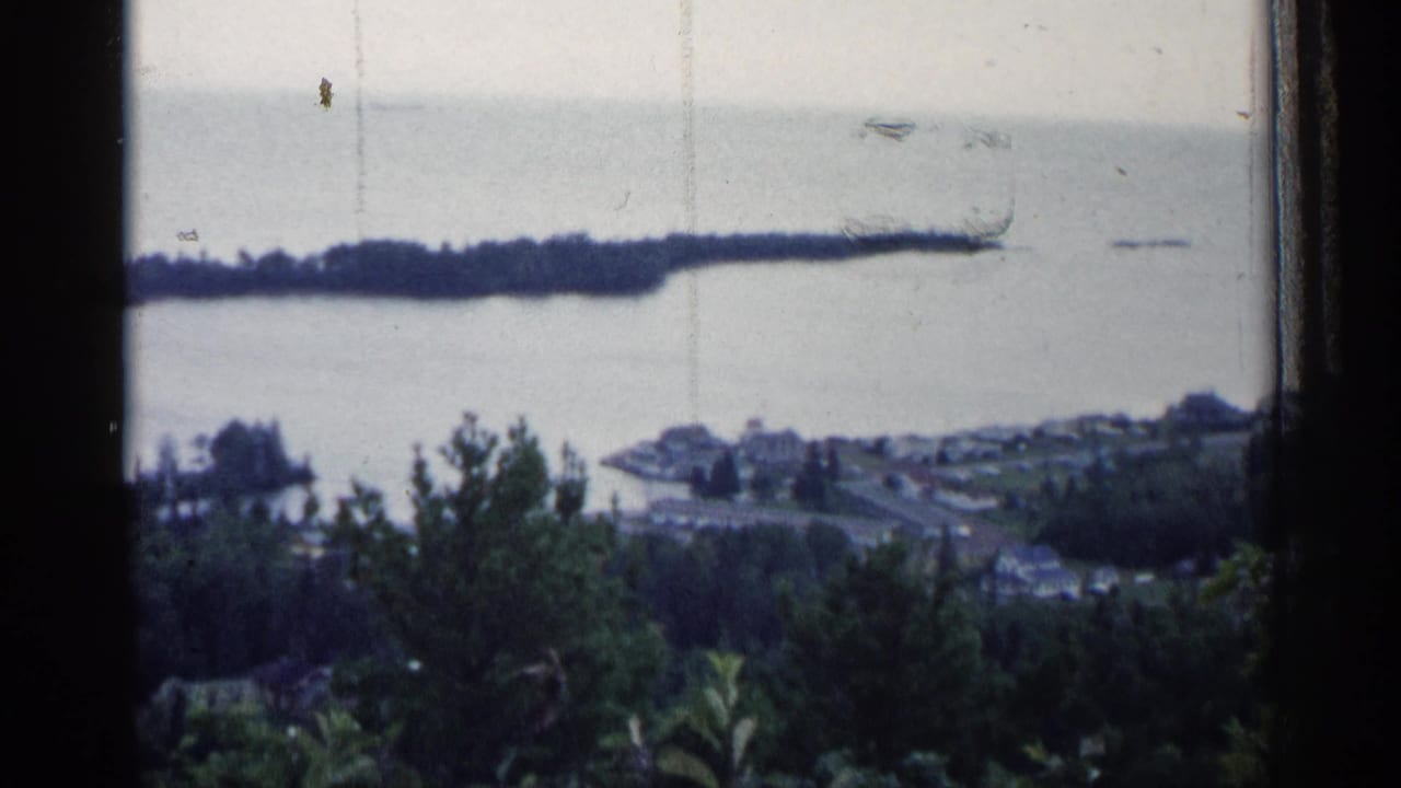 Lake overlook with wooded peninsula, waterfront buildings, foreground trees, and dark window edges.