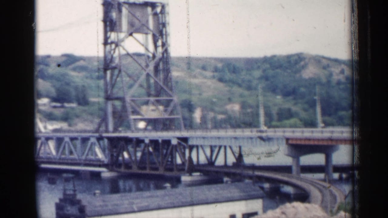 Lift bridge tower and roadway span seen across a river with hills beyond.