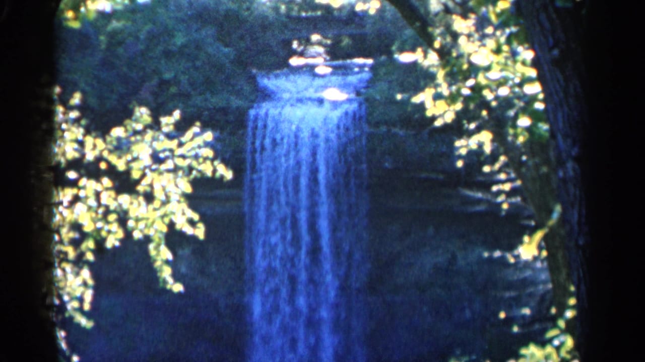 Similar waterfall view through trees with bright foliage and shaded banks.