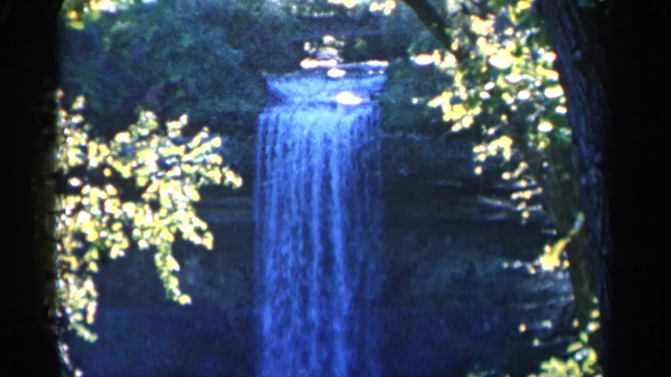 Large waterfall seen through a wooded foreground, with saturated blue water and high-contrast 8mm color.
