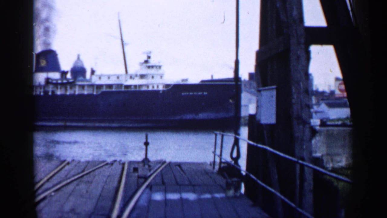 Large ferry across water viewed from a wooden pier with rails and posts.