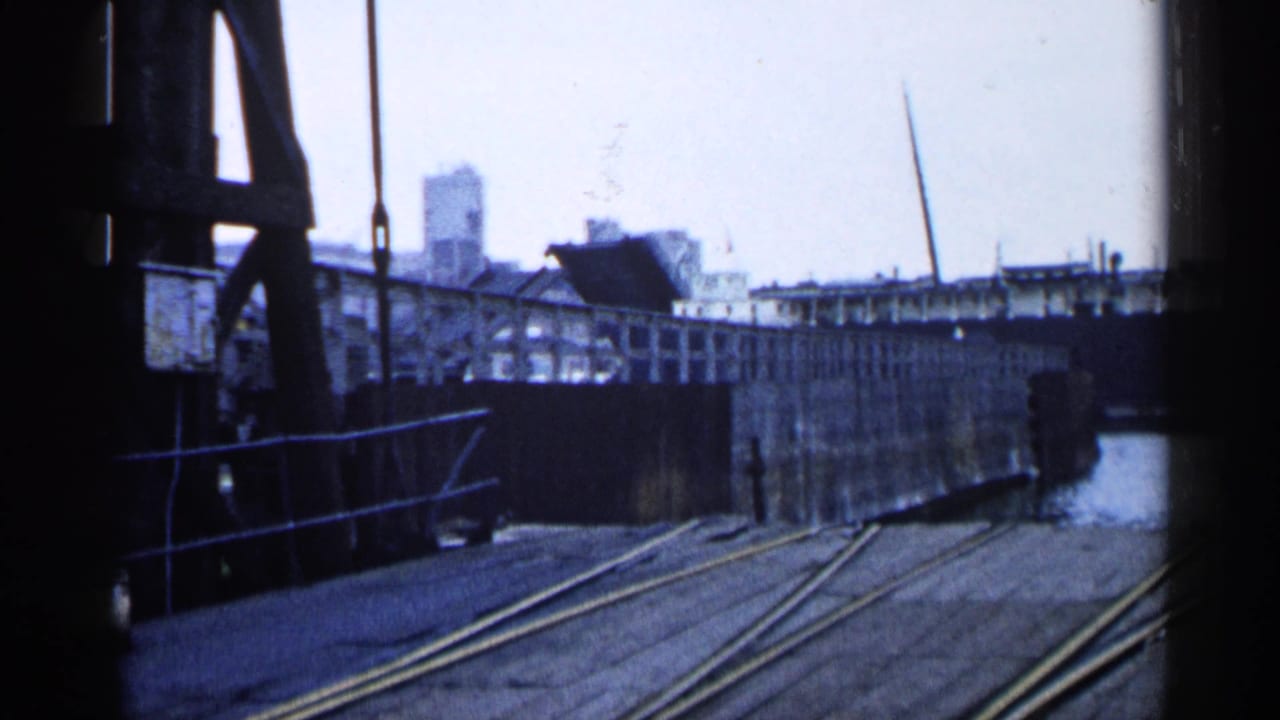 1960 Michigan dock view with rail tracks, raised bridge structure, water edge, and industrial buildings in the background.