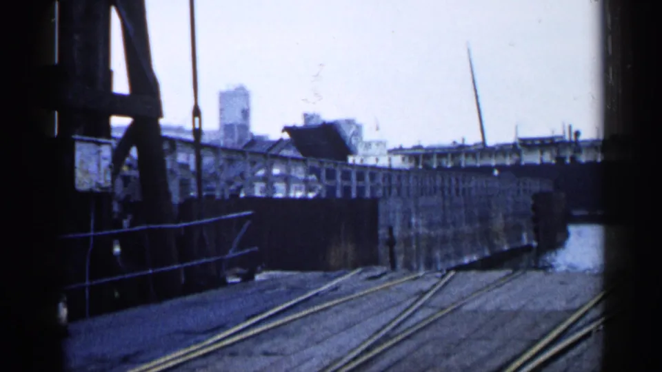1960 Michigan dock view with rail tracks, raised bridge structure, water edge, and industrial buildings in the background.