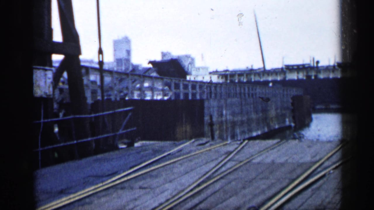 Dockside view in Michigan showing rails across the pier, a raised bridge, industrial structures, and harbor water.