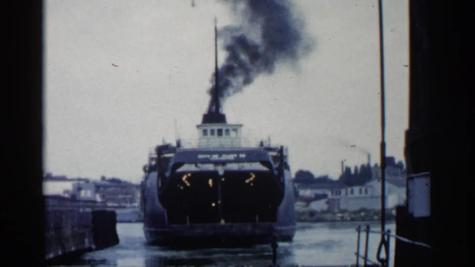 1960 Michigan 8mm frame showing the vessel aligned near the pier, with deck lights visible and dark smoke rising above the stack.