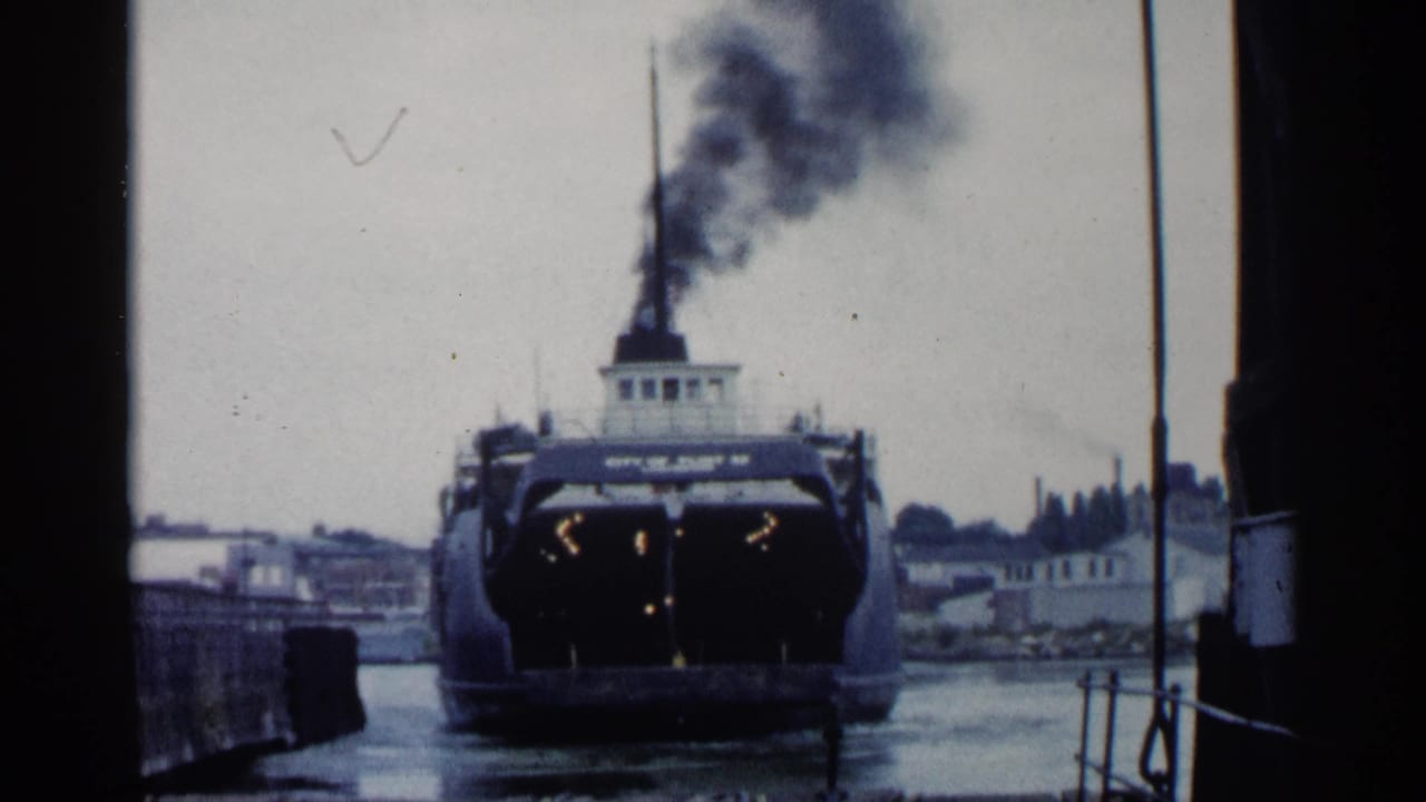 1960 Michigan 8mm frame showing a ferry or steamship near a dock, with dark exhaust above the stack and waterfront buildings behind it.