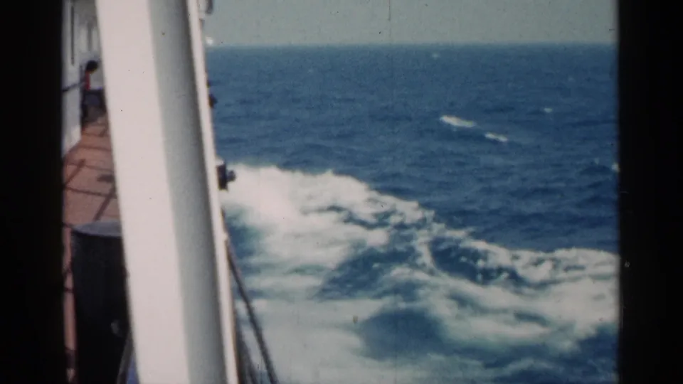 Passenger-view frame of blue water and foamy ship wake from a ferry or vessel deck in 1960 Michigan home-movie footage.