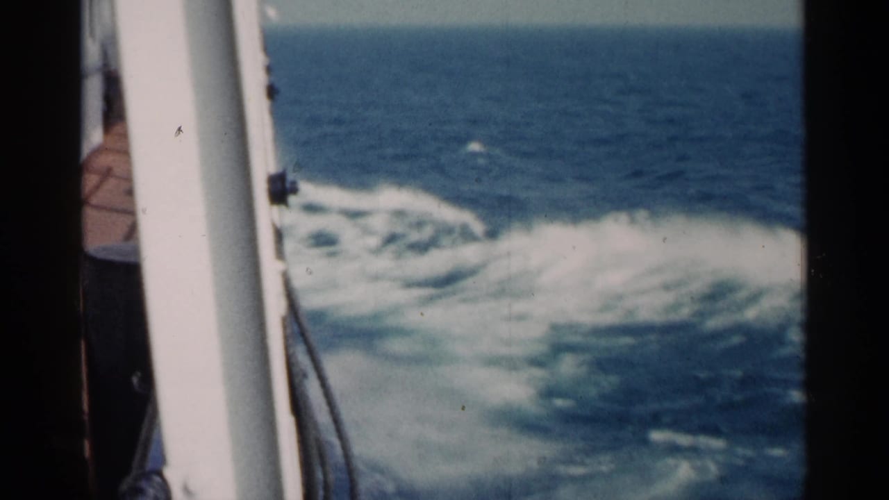 Ship deck edge and white wake foam beside blue open water.