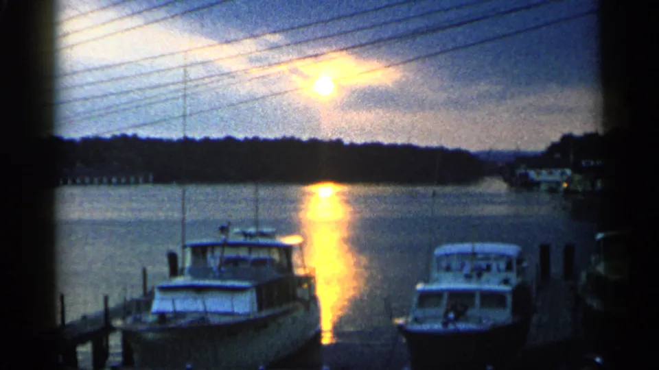 1960 Michigan 8mm frame showing docked motorboats beside a pier as the sun reflects across marina water.