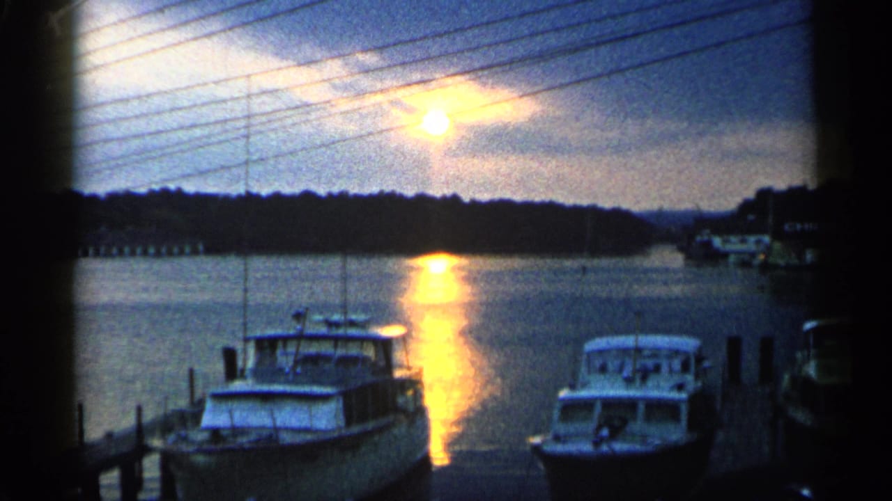 Marina boats and pier silhouetted against a bright sunset reflection.