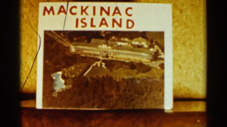 Close 8mm frame of a Mackinac Island postcard showing an aerial view, with slight film scratches and warm color cast.