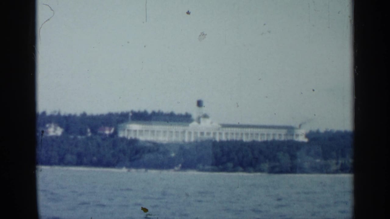 Distant long white building across water with trees along the shore.