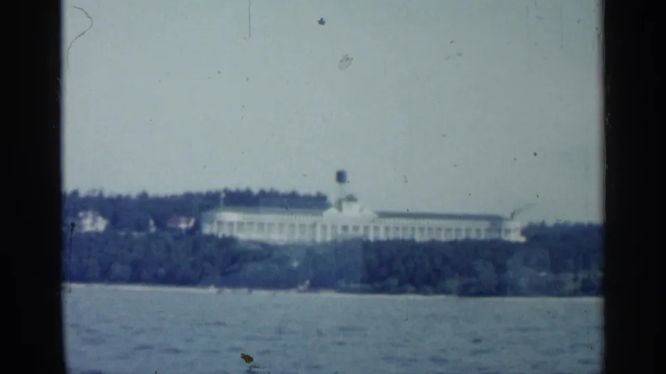 1960 Michigan 8mm frame showing a distant long white shoreline building seen from water.