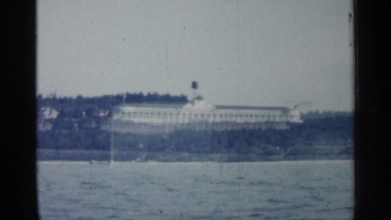 A distant shoreline building in Michigan appears across the water in faded 1960 home-movie color.