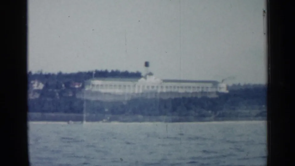 A distant shoreline building in Michigan appears across the water in faded 1960 home-movie color.