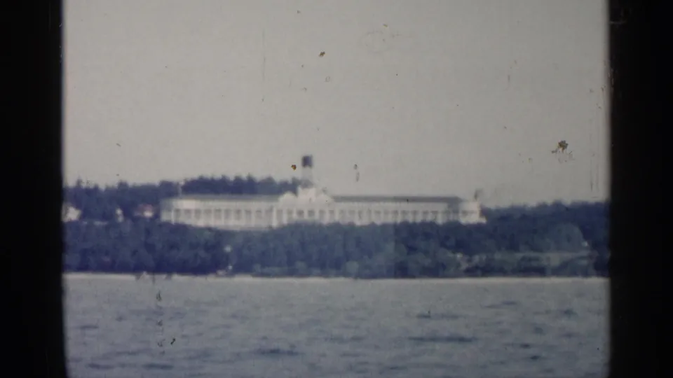 1960 8mm frame with a soft distant view of a white building on a Michigan shoreline.