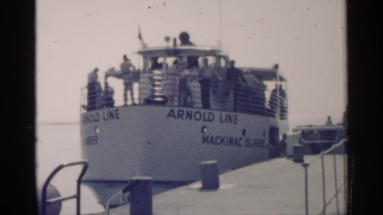 Arnold Line ferry marked Mackinac Island sits beside a pier in Michigan, with passengers standing along the deck railings.