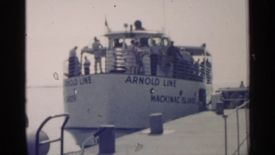The ferry stern fills the frame, showing Arnold Line lettering, deck passengers, dock railings, and a bollard near the pier edge.