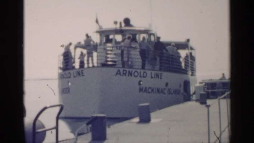 A dockside view shows the Arnold Line ferry marked Mackinac Island with passengers on deck, railings, water, and pier fittings visible.