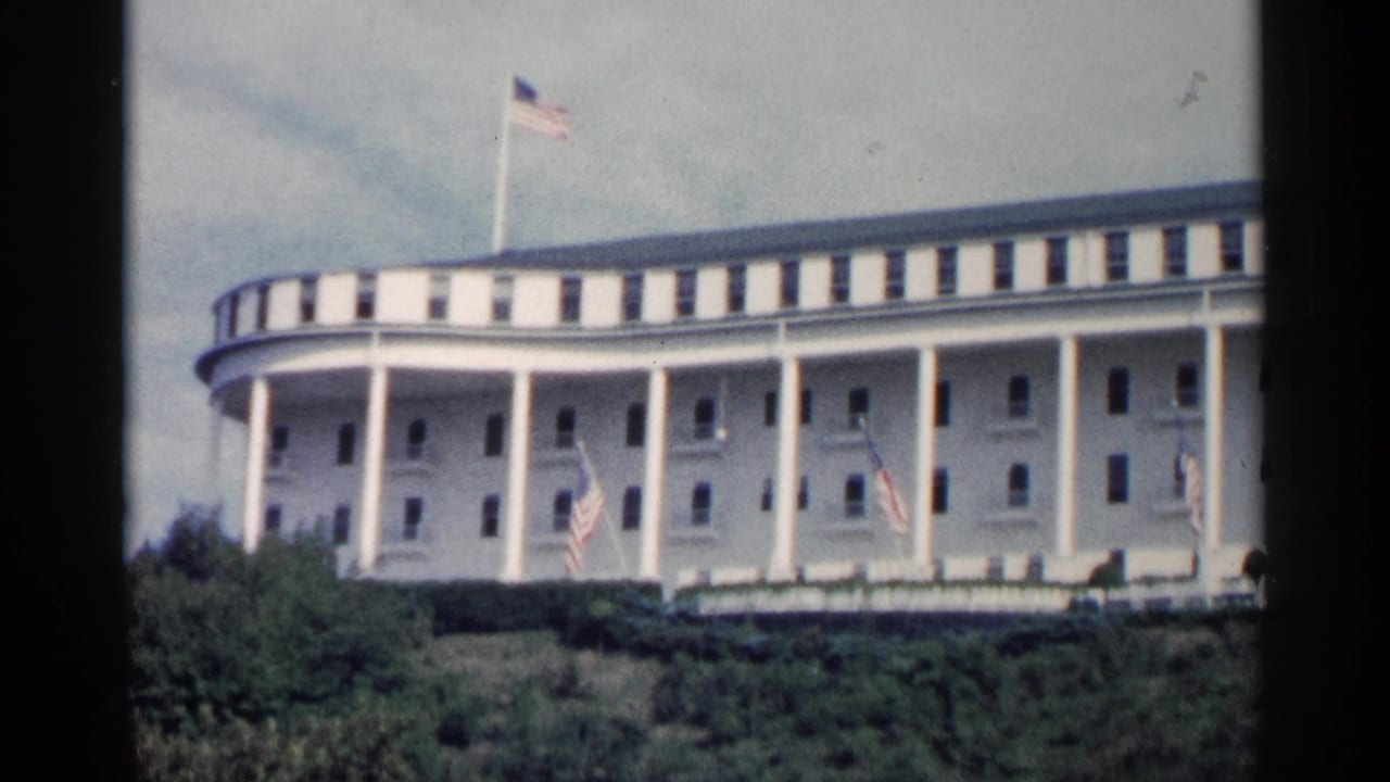 White colonnaded building with American flags and green landscaping in front.