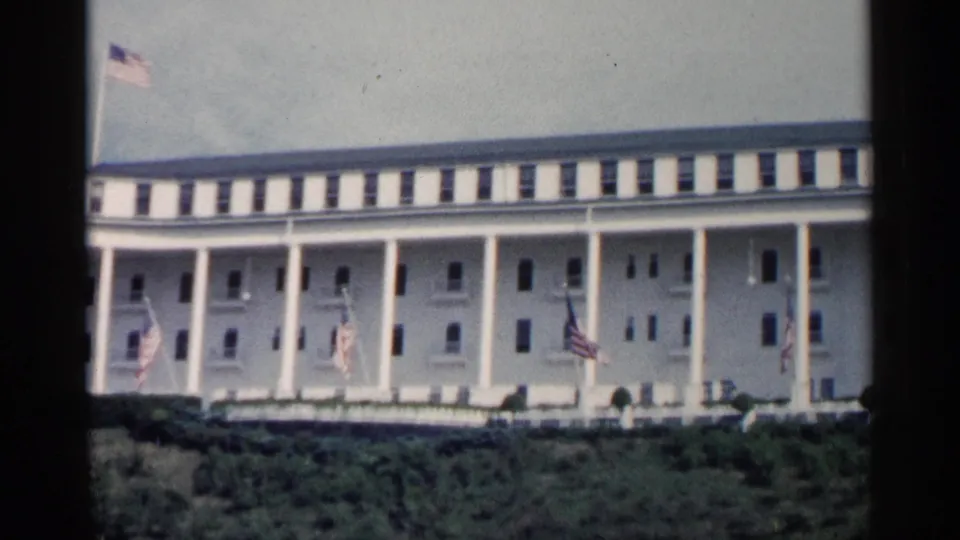 1960 Michigan frame showing the broad white facade, tall columns, American flags, landscaped foreground, and visible film gate edges.