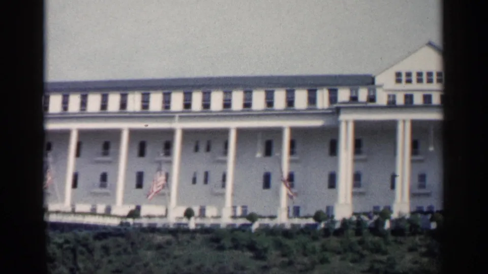 1960 Michigan frame of the colonnaded building, with American flags and a gabled end section visible.