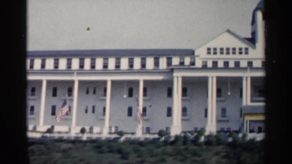 1960 Michigan 8mm frame showing the broad white colonnaded facade, flags, and gabled roof detail.