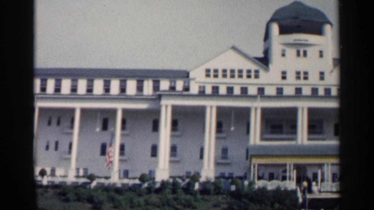 1960 Michigan exterior view of a large white resort building with a green dome, columned porch, entrance canopy, American flag, and visitors at ground level.