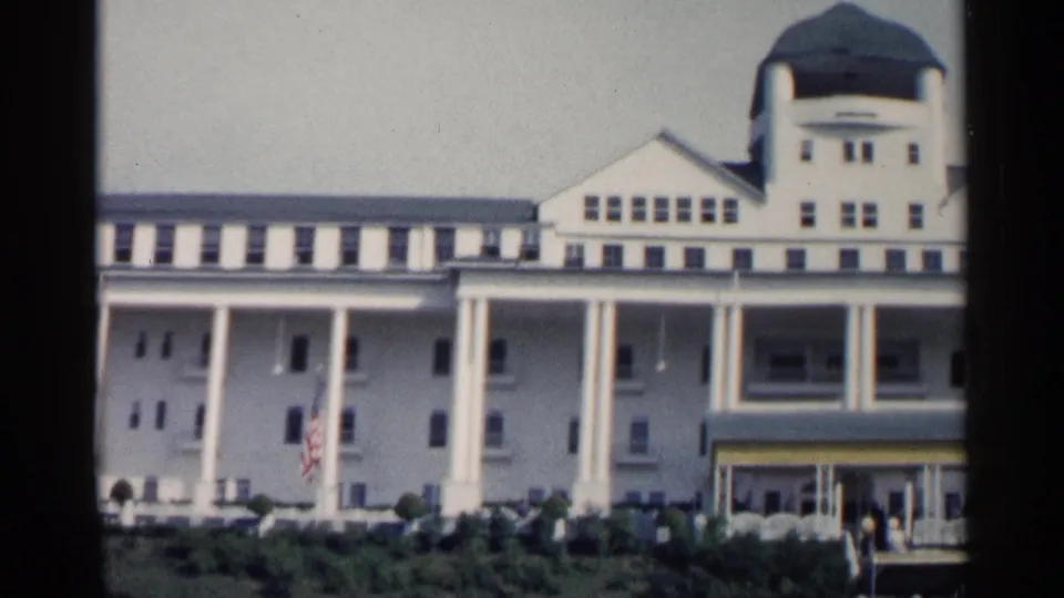 1960 Michigan exterior view of a large white resort building with a green dome, columned porch, entrance canopy, American flag, and visitors at ground level.