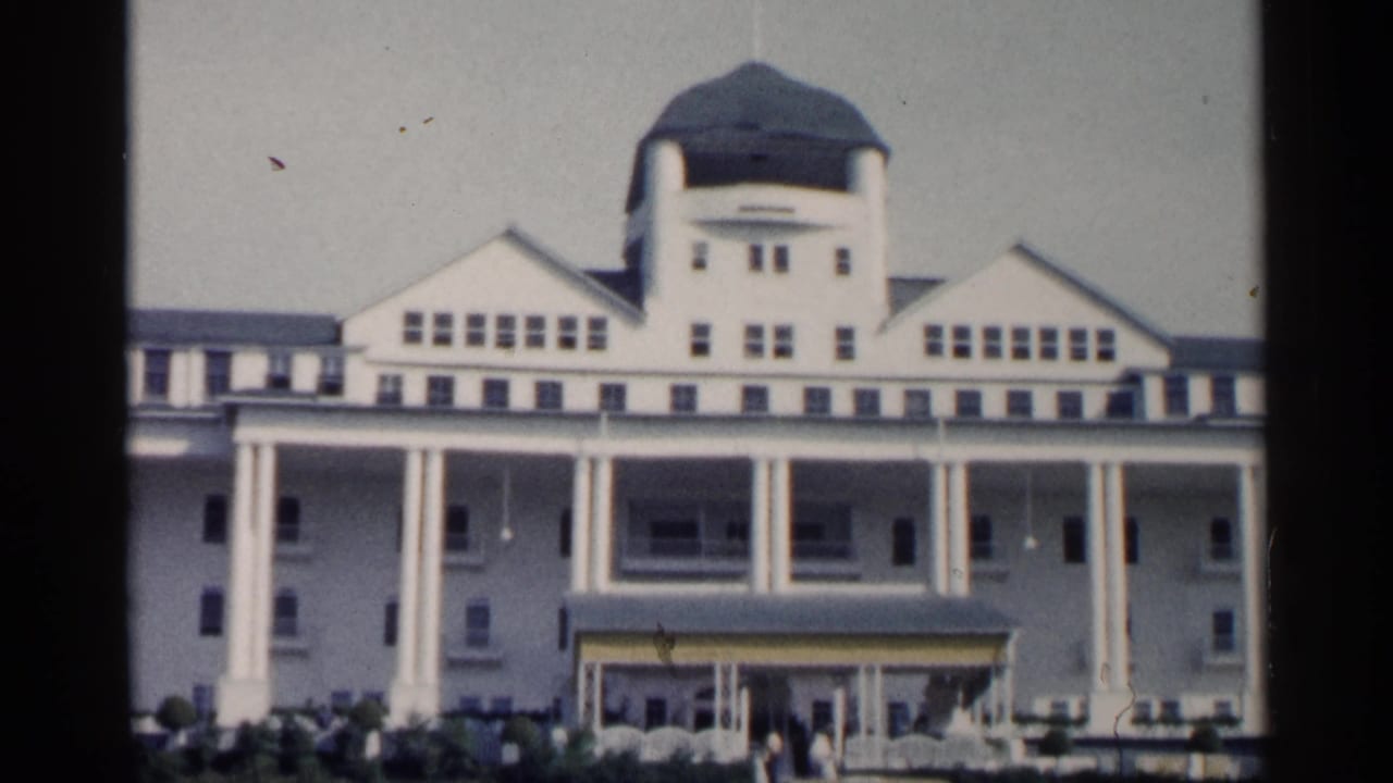 1960 Michigan 8mm frame of a white resort facade with double columns, a central domed roofline, rows of windows, and front landscaping.