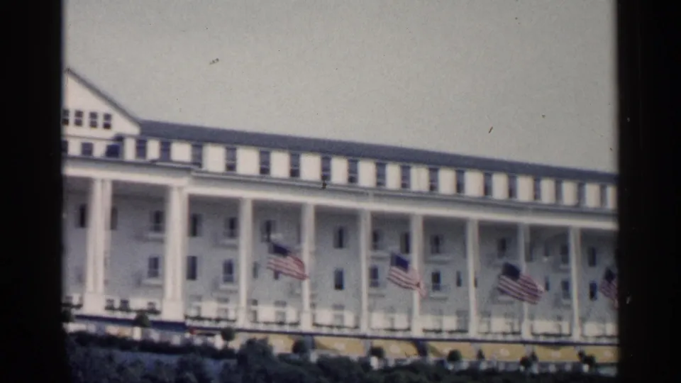 A soft 8mm view of the Michigan resort facade shows porch columns, flags, upper windows, yellow awnings, and dark foliage below.