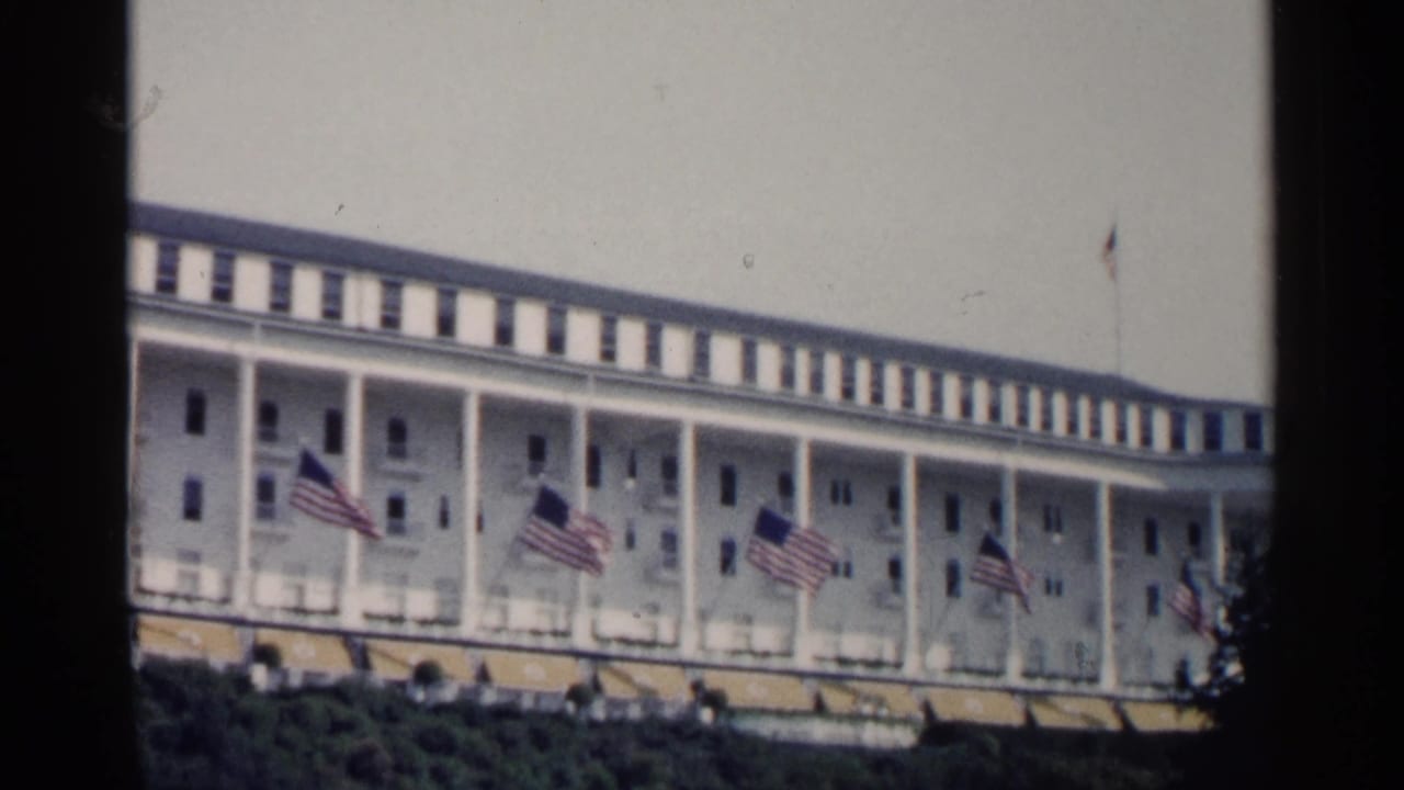 A visitor-shot 1960 Michigan resort exterior shows a white colonnaded hotel front with flags fluttering across the facade.