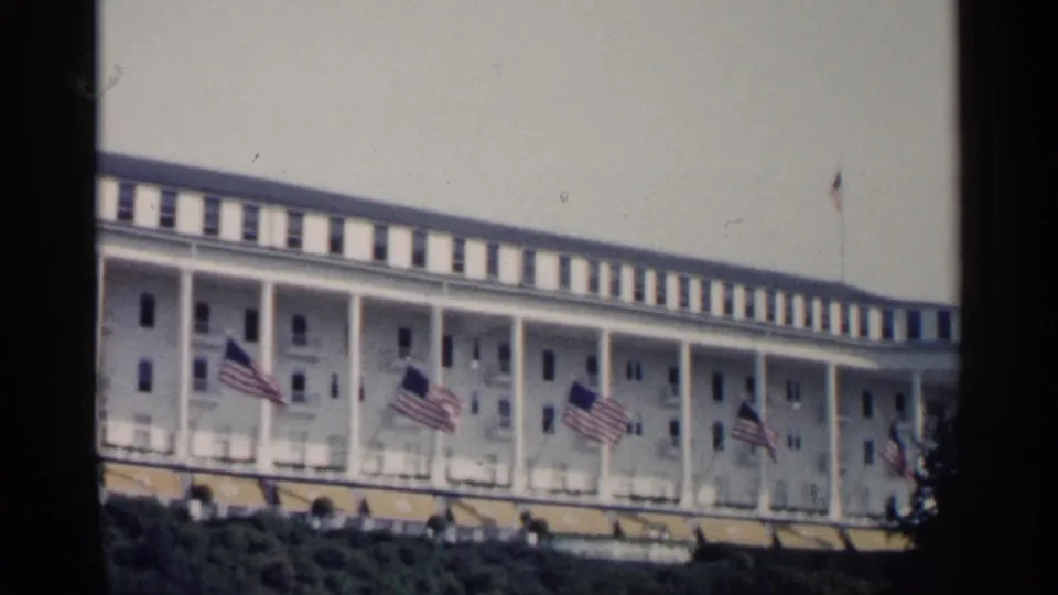 A visitor-shot 1960 Michigan resort exterior shows a white colonnaded hotel front with flags fluttering across the facade.