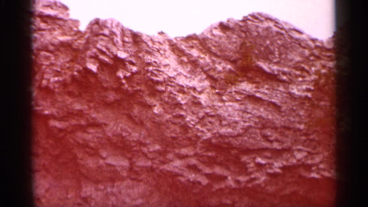 1960 Michigan 8mm frame showing a close view of rugged eroded rock with a reddish color cast and bright sky above.