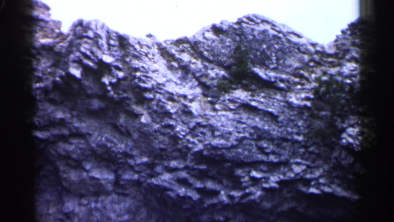 Rocky ridge with layered erosion and sparse vegetation below bright sky.