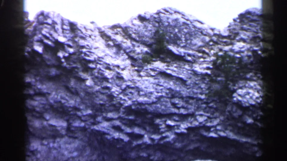 1960 Michigan 8mm frame showing a closer section of eroded rock surface with shadowed ridges and sparse vegetation.