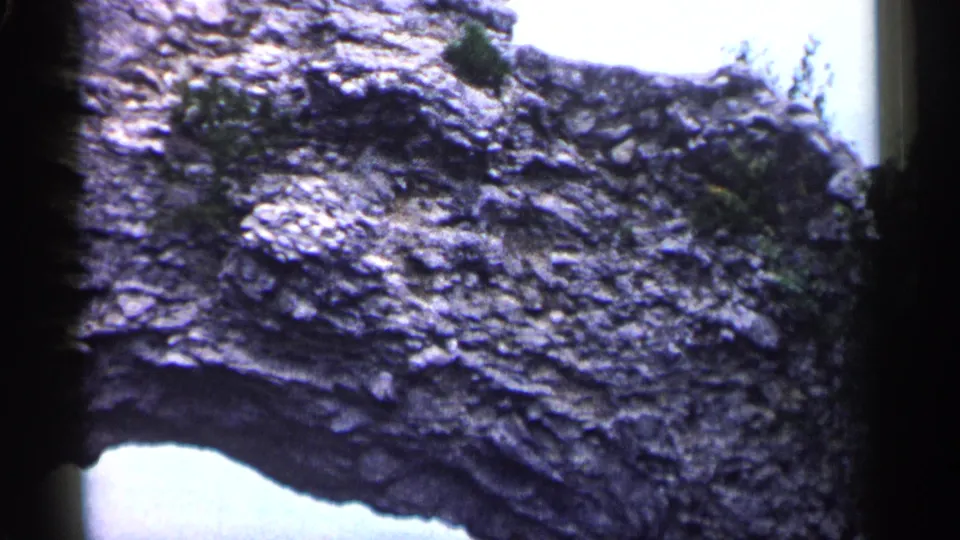 1960 Michigan 8mm frame showing a weathered rock formation, natural arch opening, and small plants clinging near the upper edge.