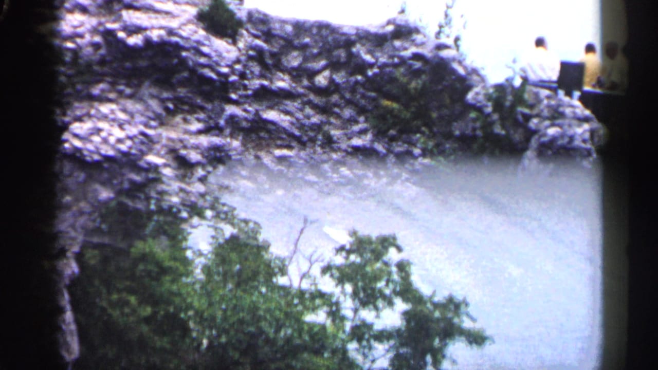 Rock ledge above pale open view with trees below and people near the top edge.