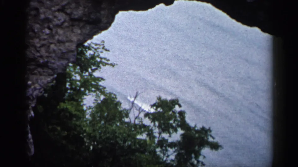 1960 8mm Michigan frame looking through a natural rock arch toward green trees and a pale distant view.